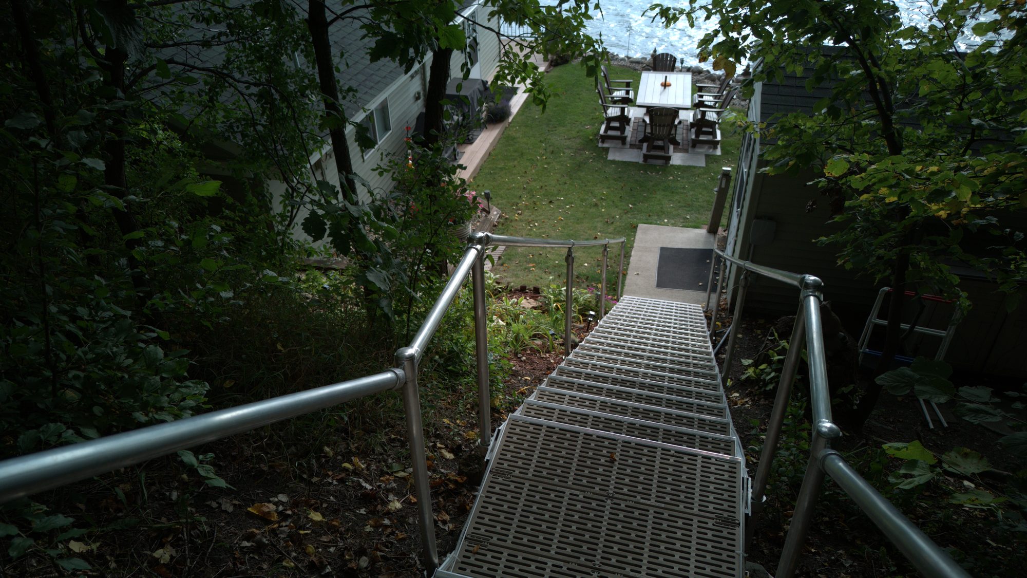 Aluminum stairway descending a wooded slope to a lakeside patio